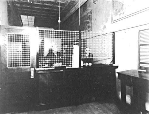 Clerks wait behind a counter shielded with a metal grate.